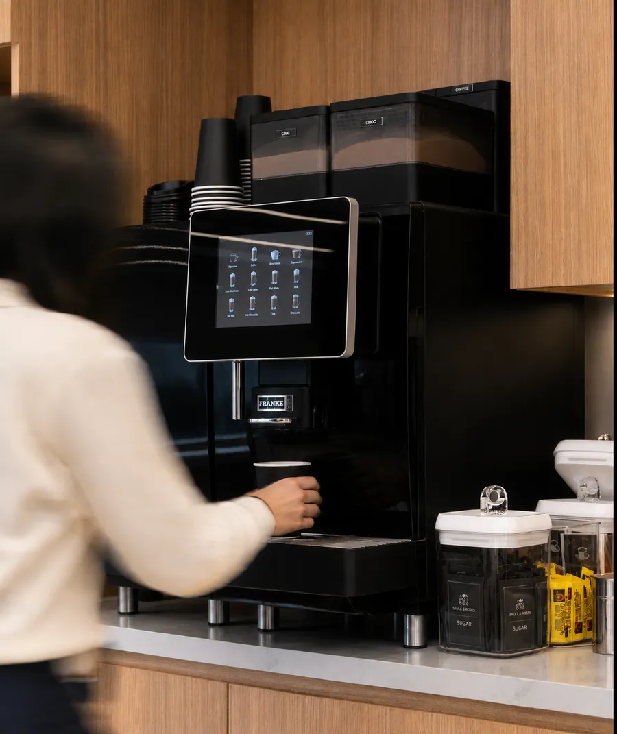 Someone taking a cup from a bean-to-cup machine at an office coffee point stocked with Skull & Roses sugar